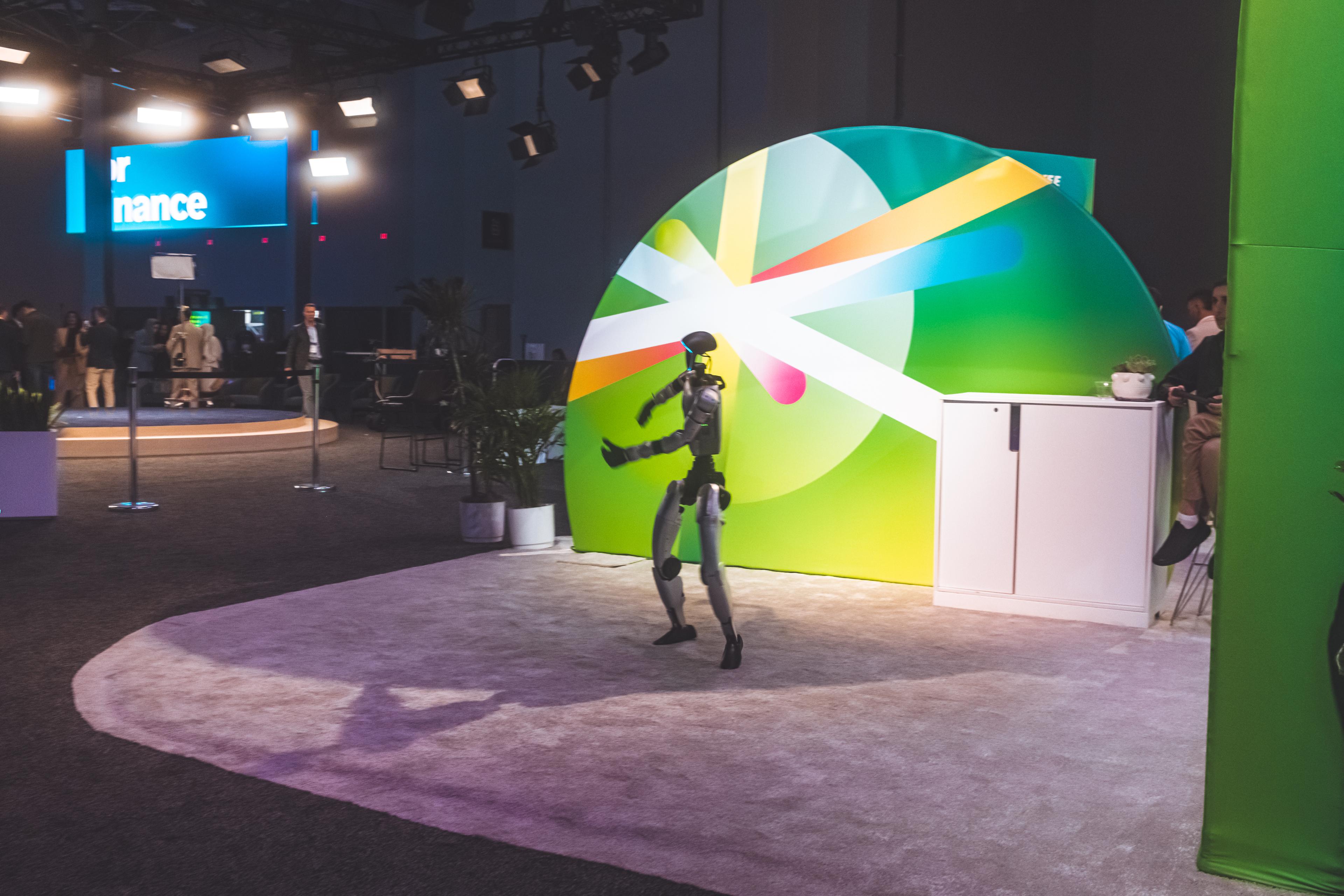 Humanoid robot walking the convention expo floor in front of a large colorful dome backdrop
